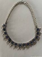 Full view of silver flower necklace with blue stones along the chain and hanging elements, showing design and condition.