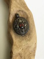 Front view of oval Bali style silver pillbox pendant with central oval garnet and decorative silver motifs.