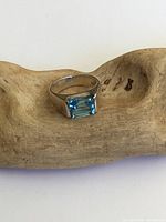 Front view showing rectangular cut blue gemstone with bright medium blue color set on a polished sterling silver band with visible tarnish and surface wear.