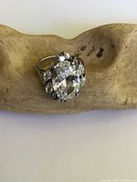 Front view of sterling silver cocktail ring with large oval clear crystal and smaller surrounding crystals on a rustic wood surface