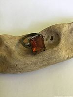 Front side angled view of sterling silver ring with rectangular orange gemstone set in prongs on silver band showing tarnish and surface wear.