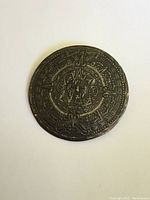 Front view of round silver brooch/pendant with intricate Mayan design on the face, showing dark tarnish and detailed etching.