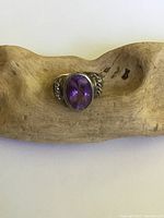 Front view of sterling silver ring with oval purple faceted crystal set in bezel, shown on wooden background.