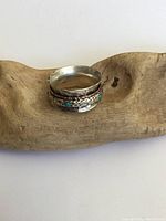 Vintage sterling silver and turquoise spinner ring displayed on natural wood background, showing the hammered texture and turquoise stones in close-up.