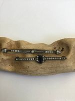 Front view of two antique sterling silver Art Deco brooches placed on carved wooden display, showing clear and blue glass stones and filigree silver detailing.