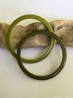 Pair of vintage Bakelite bangles: one olive green and one darker green lying flat on rustic wood for display.