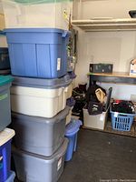 Five stacked storage bins of different sizes and colors in garage, mostly Rubbermaid brand