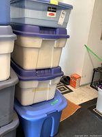 Photo showing stacked storage bins, two beige with purple lids, and two blue bins, one with a blue lid, visible dirt and wear.