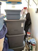 Stack of 3 large grey Rubbermaid bins with blue Sterilite bin on top and nearby open bin.