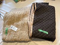 Handmade beige throw blanket and folded dark grey quilt with beige edging side by side on a surface.