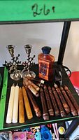 Photo showing white battery operated taper candles, wooden taper candles, two metal candle holders with snowflake designs, two metal wall sconce candle holders, and a bottle of Lamp Berger cinnamon roll oil.