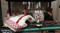 Shelf display showing several Christmas figurines including Santas and angels, a Christmas tree skirt folded, a serving platter, and signs.