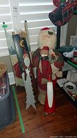 Photo shows three Christmas statuettes: a large Santa holding a smaller Santa, a wooden Santa figure in red, and two wooden paintings in the background with Christmas themes.