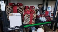 Photo showing two woven gift box Christmas decorations with red ribbons, snowman figurine, pinecone wreath, white pinecone ornament, and some glass baubles on a black shelf.