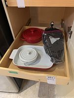 Ceramic cooking ware including red casserole dish with lid, white ceramic lidded dish, a ceramic baking dish, and a coffee press sealed in plastic.