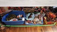 Overview of fall decor lot showing blue bin with pumpkins, welcome sign, pinecones, and bags of various decorative items including faux leaves and berries, plus a box of artificial orange flowers.