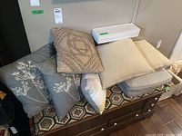 Seven decorative pillows arranged on a patterned surface including multiple colors and styles