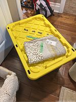 Large yellow storage bin filled with queen size sheets, with one folded sheet on top showing beige and patterned details.