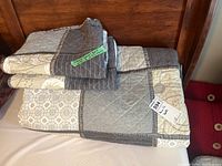 Folded patchwork quilt laid on bed showing various block patterns in gray, beige, and cream with a quilted texture.