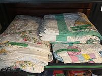 Four folded quilts with handwritten green tape labels describing them as machine pieced and quilted.