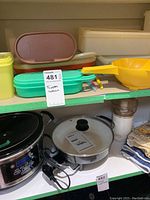 Shelf containing assorted Tupperware containers in various colors and lids along with kitchen appliances and textiles below
