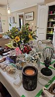 Wide view showing assortment of vases, artificial flowers, shells in jars, and battery operated cage light on table.