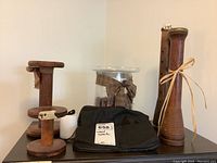 Lot with four wooden spools, one large clear glass container filled with pine cones and decorated with a brown checked fabric bow, and a black cloth bag with metal star and tree shapes.