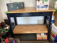 Front view of the wood framed work bench showing butcher block style top, blue painted frame with one drawer, and slatted wooden bottom shelf.