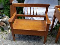 Front view of oak hall bench showing spindle backrest, armrests, and hinged seat lid