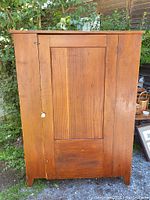 Front view of antique pine cupboard showing door and paint finish under natural light outdoors.