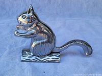 Side view of shiny metal squirrel nutcracker showing detailed features and tail extending backwards.
