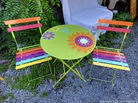 Full view of the metal bistro set showing round floral table and two multicolor folding chairs set outdoors.