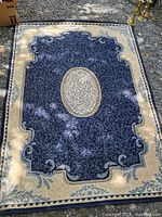 Full view of the deep blue and cream carpet with detailed scrolling floral and ornamental design and central oval medallion.