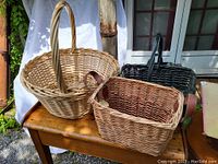 Front side view of 3 large bamboo/rattan market baskets showing one round bamboo basket with handle, one rectangular rattan basket with leather handles, and one black rectangular rattan basket.