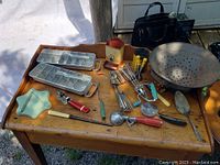 Photo showing two aluminum ice cube trays, tin colander, hand-crank egg beaters, glass star-shaped dish, and assorted vintage kitchen tools on wooden table.