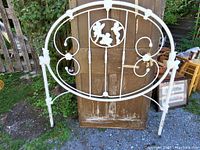 Full front view of large metal bed headboard showing the entire piece with decorative cherub design in center oval, floral and scrollwork details, painted white.