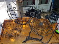 Three black metal wire flower baskets on wooden table, showing details and size