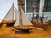 Photo showing all three wooden model boats on wood surface against a window and wall background.