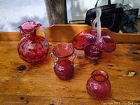 Four cranberry glass pieces on wooden table, well lit showing color and details.