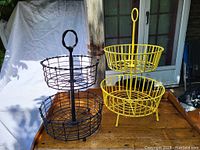 Pair of two-tiered metal countertop fruit holders, one black and one yellow, showing overall condition and size.