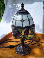 Full view of stained glass lamp showcasing floral pattern with white and multicolored glass pieces and antique bronze base.