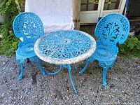 Photo showing the full bistro set including one round table and two chairs with ornate blue painted aluminum design on gravel surface.