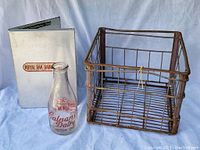 Photo displaying vintage glass milk bottle with Calnan Dairy Picton Ont. red logo, aluminum binder labeled Royal Oak Dairy Ltd., and a rusted metal milk crate showing wear and use.