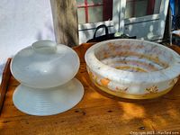 Two vintage hanging lamp shades on a wooden table, one small frosted glass and one larger with bird decoration.