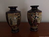 Pair of Asian inspired vases displayed side by side on a wooden surface, showing front scenes and overall shape.