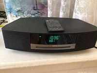 Front view of main unit with remote on top, display showing time and FM frequency