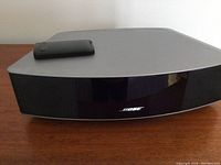 Front view of Bose Wave unit showing silver top, black front grille with Bose logo and remote on top