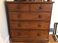 Front view of brown wooden chest of drawers with six drawers and round knobs, showing wood grain and finish condition.