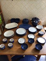 Full set of Denby Ware dinnerware pieces spread on wooden table, including serving dishes, mugs, plates, bowls, teapot, and casserole dish.