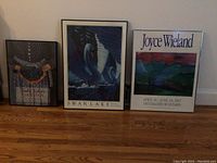 Photo showing three framed art pieces on the floor, including Swan Lake poster, Joyce Wieland poster, and a floral themed print.